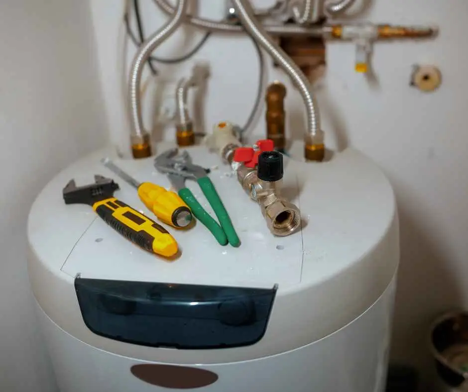 Top of a white water heater with exposed pipes and valve fittings; a yellow utility knife, green pliers, and a wrench rest on the unit.